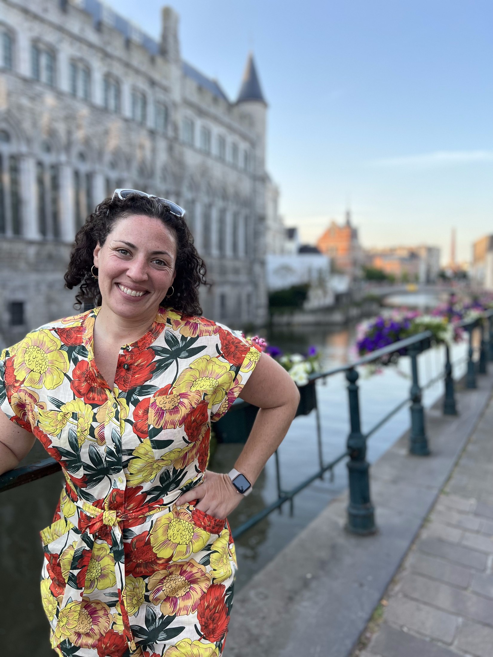 Jackie smiling on a canal bridge in Ghent, Belgium, a historic stone tower in the background.