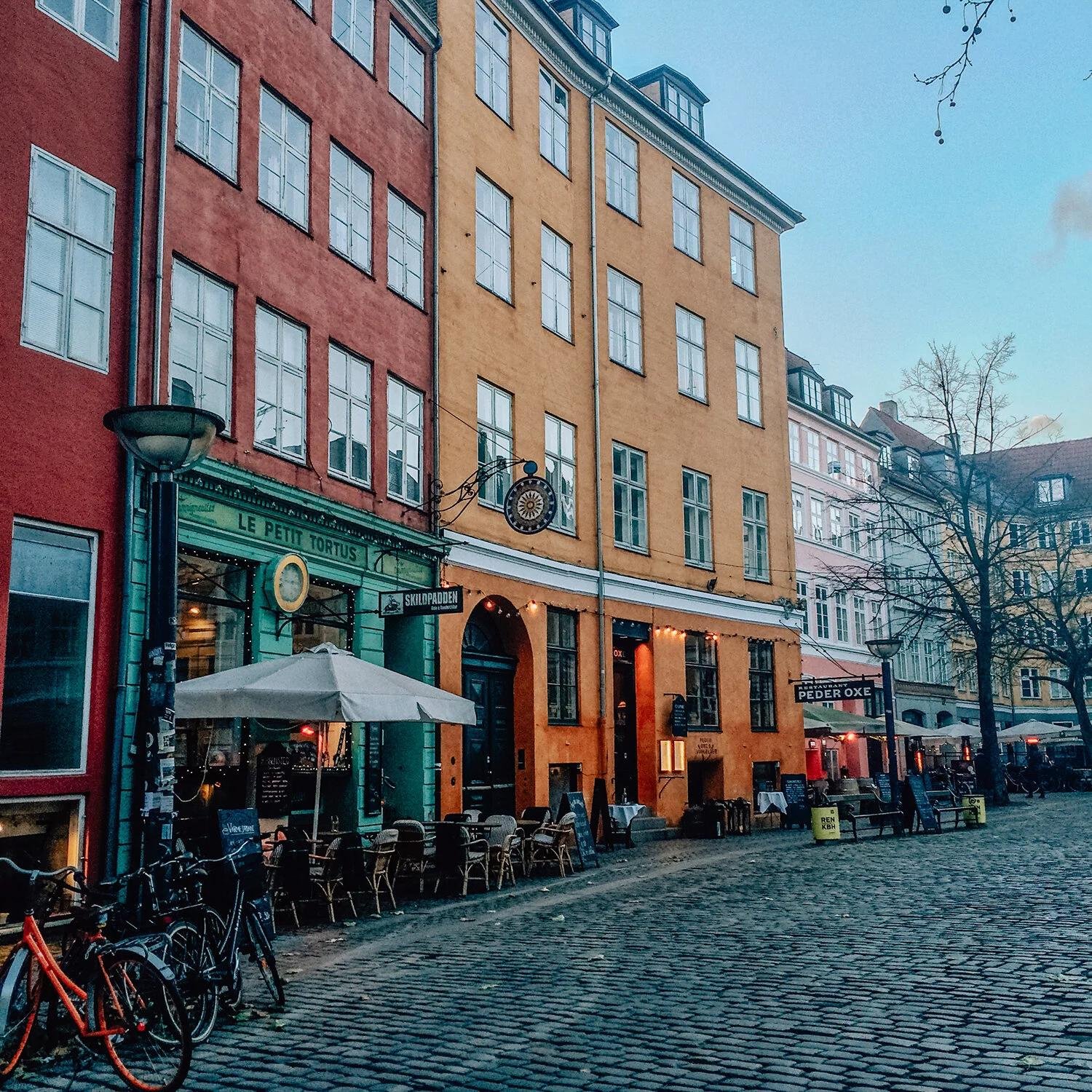 A colorful square of café-lined buildings in Copenhagen, bikes parked out front, early evening light.